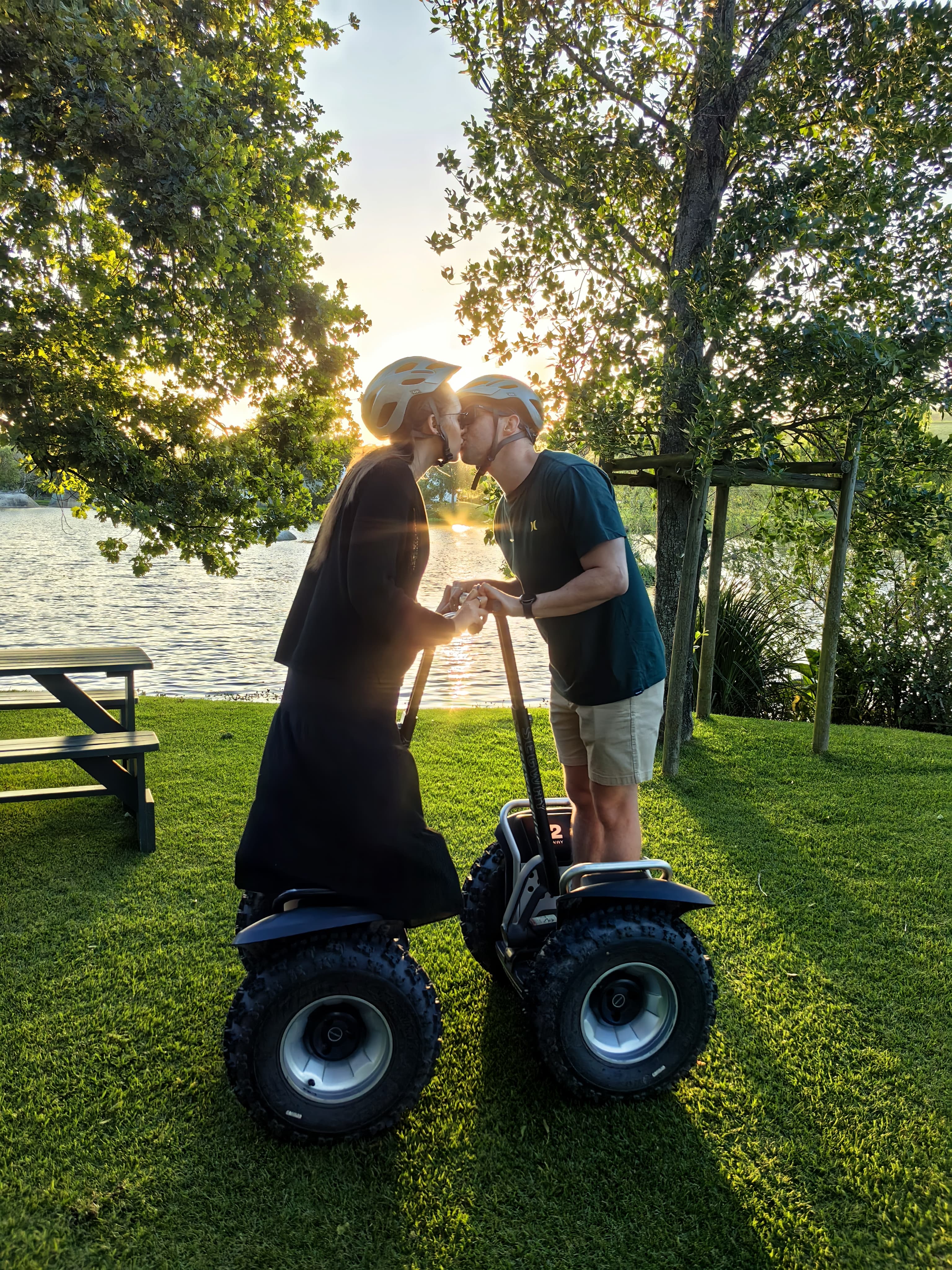 A couple sharing a kiss on segways at golden hour beside a lake during a custom GSW tour