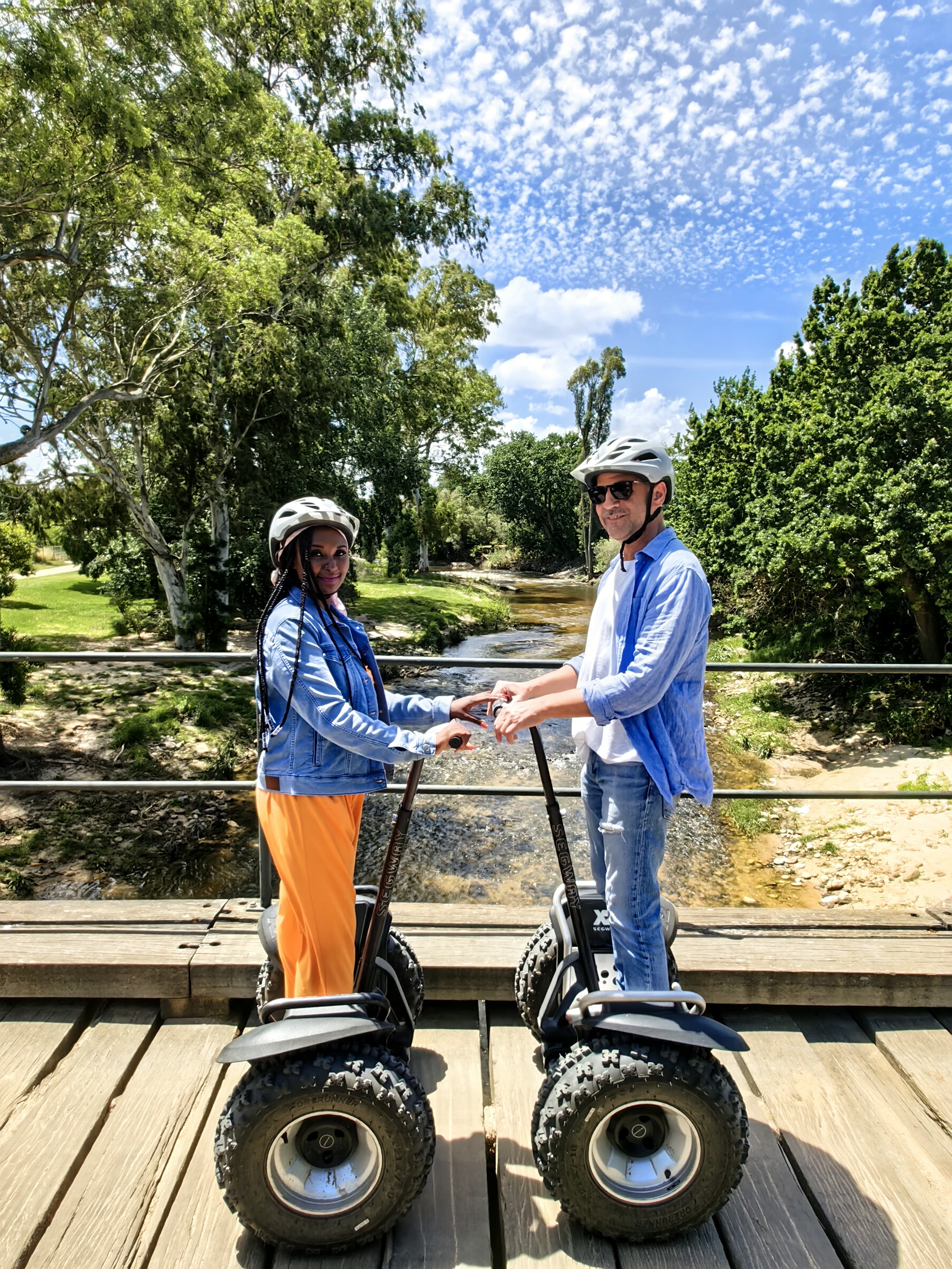 Two GSW guests on segways holding hands on a wooden bridge over a river